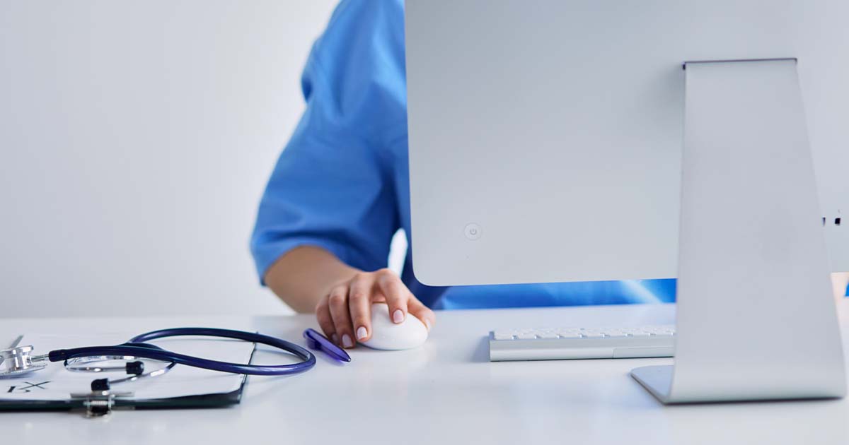 Nurse sitting at a desk with a desktop computer.